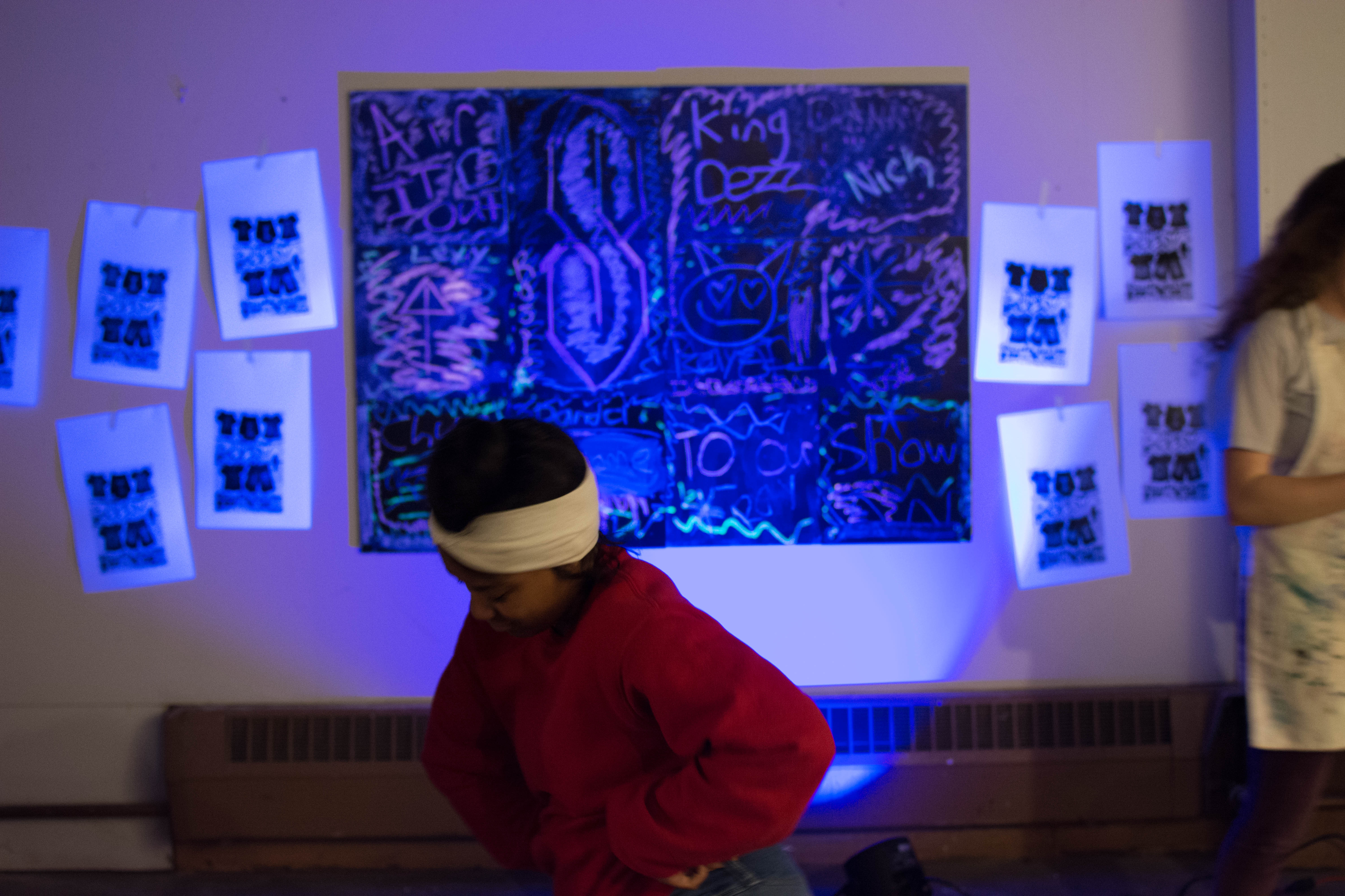 picture of teen dancing in front of black light chalk installation at Air It Out teen art exhibit