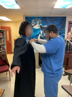 Jail students help each other try on their new Metro Panthers leather graduation gown.